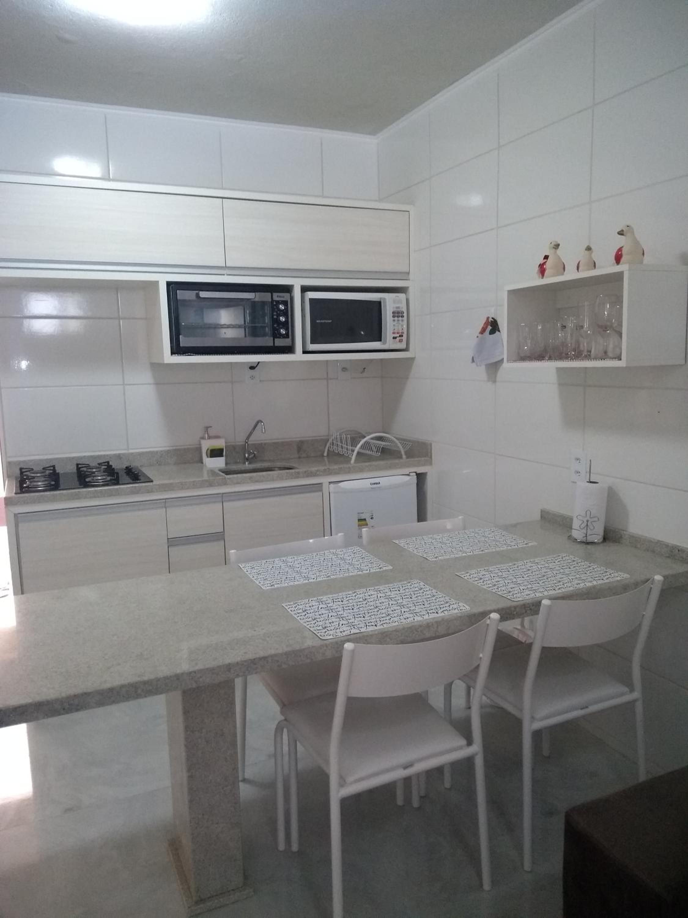 Cozinha branca do Apto 6: cooktop, micro-ondas, forno e mesa de granito
