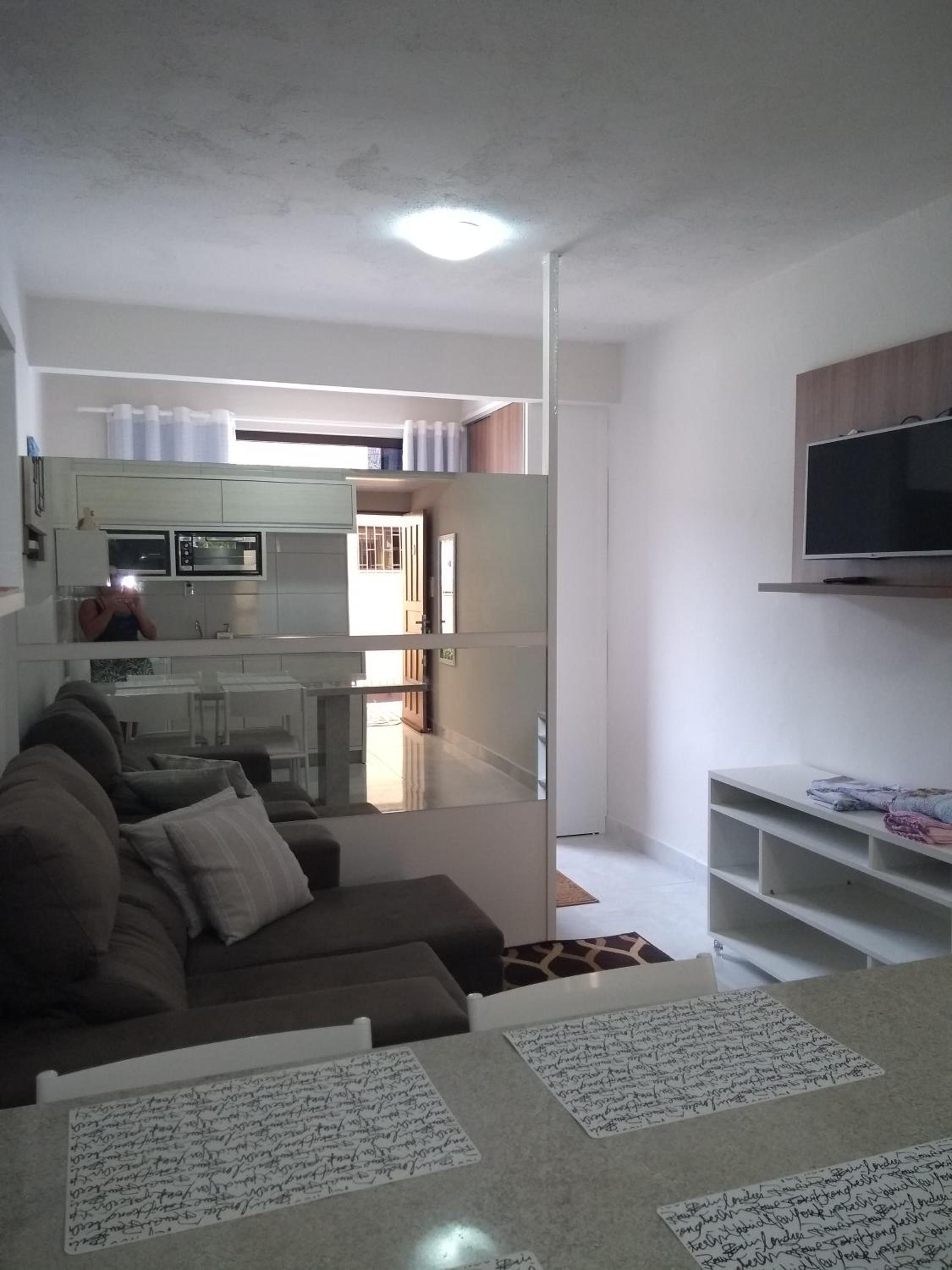 Sala do Apto 6 com sofá, TV em suporte na parede e a cozinha na mesma peça