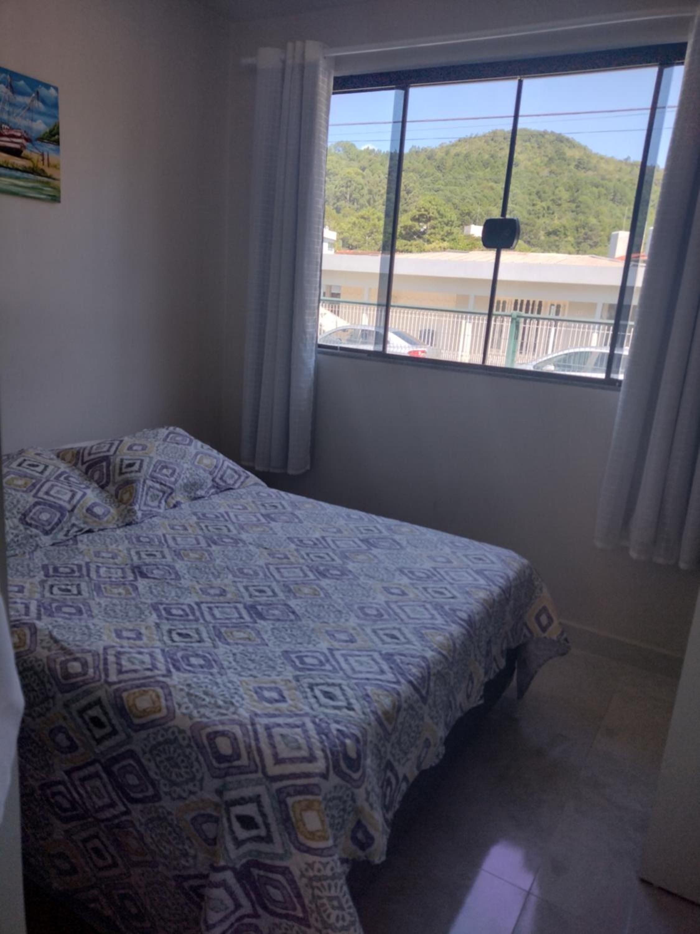 Quarto do Apto 6 com cama de casal e janela ampla para o morro verde