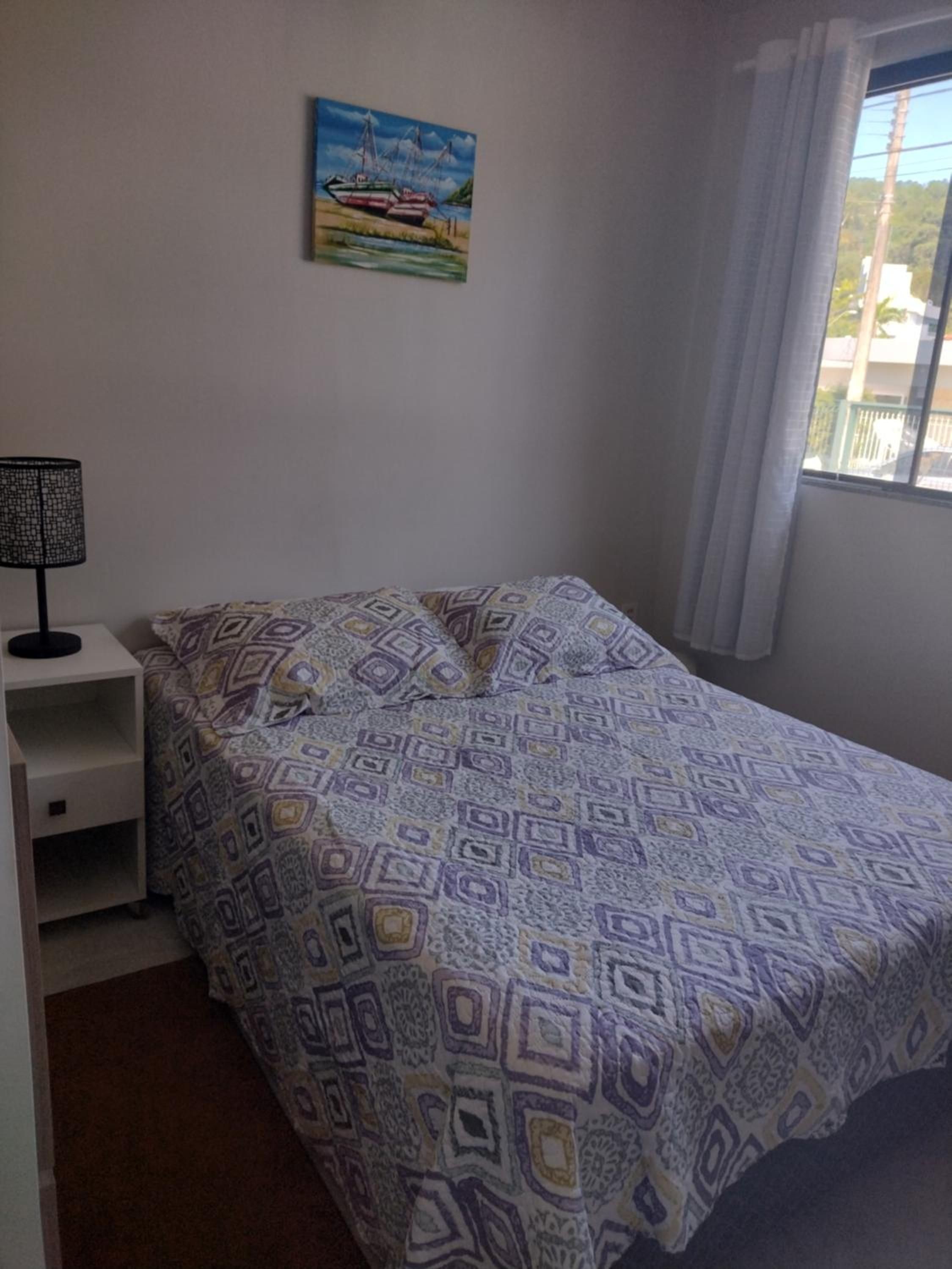Cama de casal do Apto 6 com colcha estampada, criado-mudo e abajur