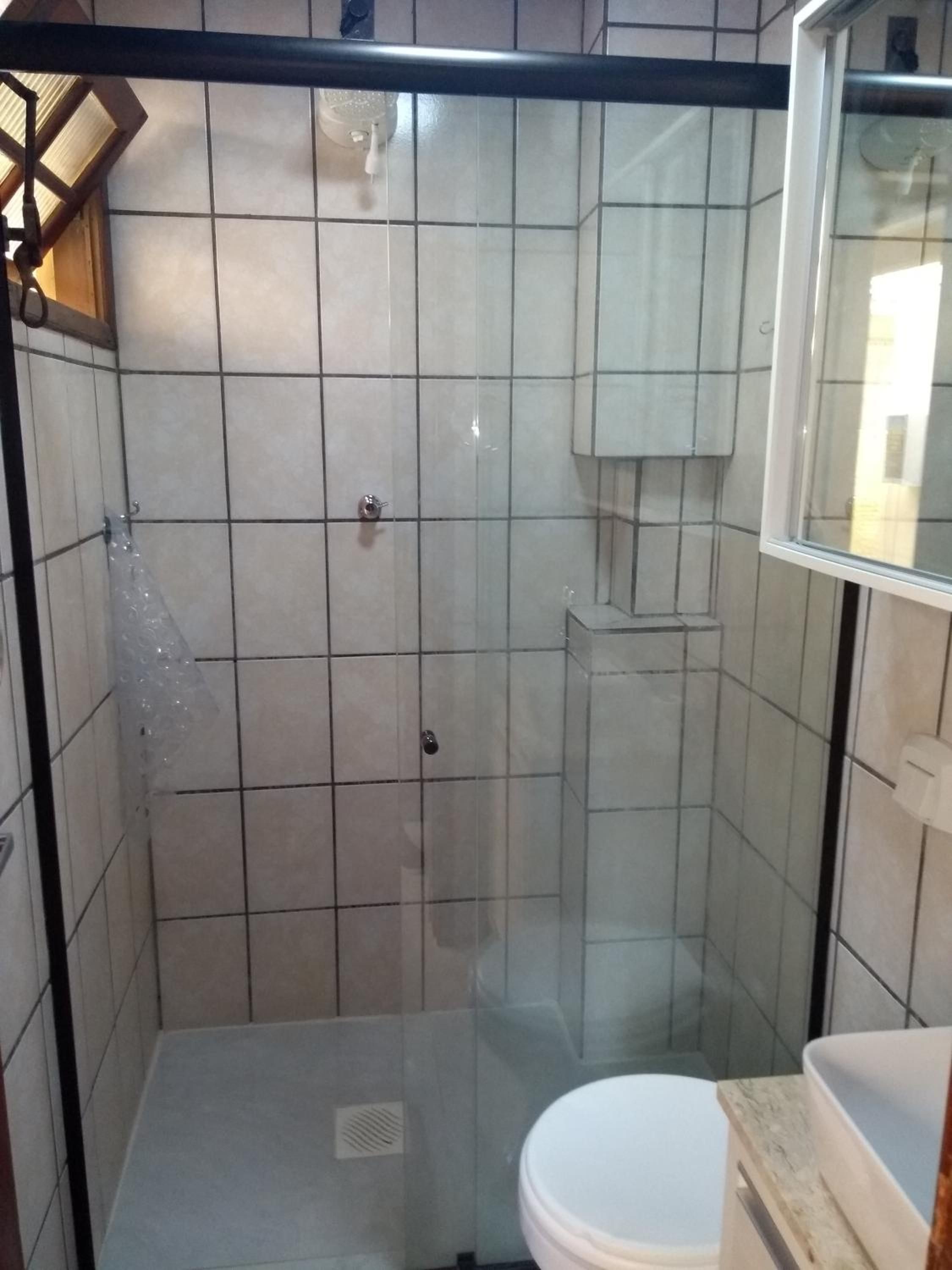 Banheiro do Apto 6 com box de vidro, vaso e azulejos claros